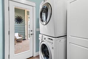 A laundry room with stacked washing machines and a door leading to a patio area with a chair and a decorative sun wall.
