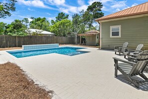 A backyard with a rectangular pool, a wooden deck, and Adirondack chairs.