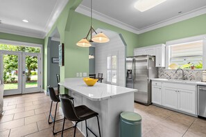A modern kitchen with a central island, bar stools, a stainless steel refrigerator, and a herringbone tile backsplash.