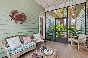 A covered patio with wicker furniture, a large window, and a decorative crab wall art piece.