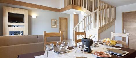 Un coin repas avec une table dressée pour deux personnes, des chaises en bois, un lustre et un escalier avec des rampes en bois.