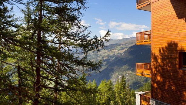 A wooden building with balconies overlooking a mountainous landscape.