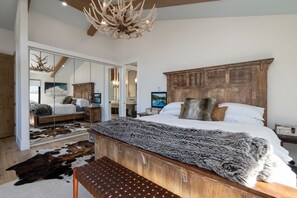 Ein Schlafzimmer mit einem großen Bett, einem Holz-Kopfteil und einem Spiegel. Im Raum befindet sich eine Bank und ein Kuhfellteppich.