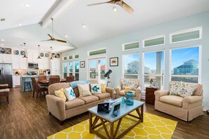 A spacious living area with a sofa set, a coffee table, and a dining table. There are multiple windows providing natural light and views of the outside. - Sweetsol 4 Bedroom Home by RedAwning (Port Bolivar)