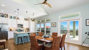 A spacious kitchen with a large island, white cabinetry, and a dining area with wicker chairs.