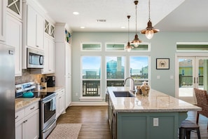 A kitchen with white cabinets, a large island, a microwave, and a view of the outside. - Sweetsol 4 Bedroom Home by RedAwning (Port Bolivar)