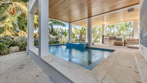 A modern outdoor pool area with a wooden ceiling, surrounded by tropical plants and a view of the ocean. - Rooftop deck with Gulf views - Villa Rayo Del Sol (Bradenton Beach)