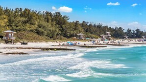 A beach with lifeguard towers, beach umbrellas, and people enjoying the shore. - Rooftop deck with Gulf views - Villa Rayo Del Sol (Bradenton Beach)