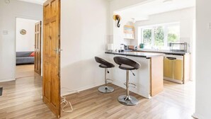 A modern kitchen with a wooden door, two bar stools, and a window providing natural light. - Spacious 3bhk Near Heathrow (Hounslow)