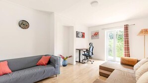 A modern living room with a grey sofa, a brown sofa, a desk with a chair, and a large window with curtains. - Spacious 3bhk Near Heathrow (Hounslow)