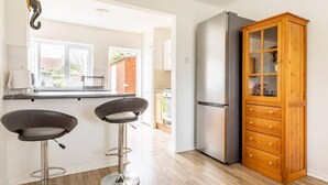 A modern kitchen with a stainless steel refrigerator, wooden cabinet, and two bar stools. - Spacious 3bhk Near Heathrow (Hounslow)