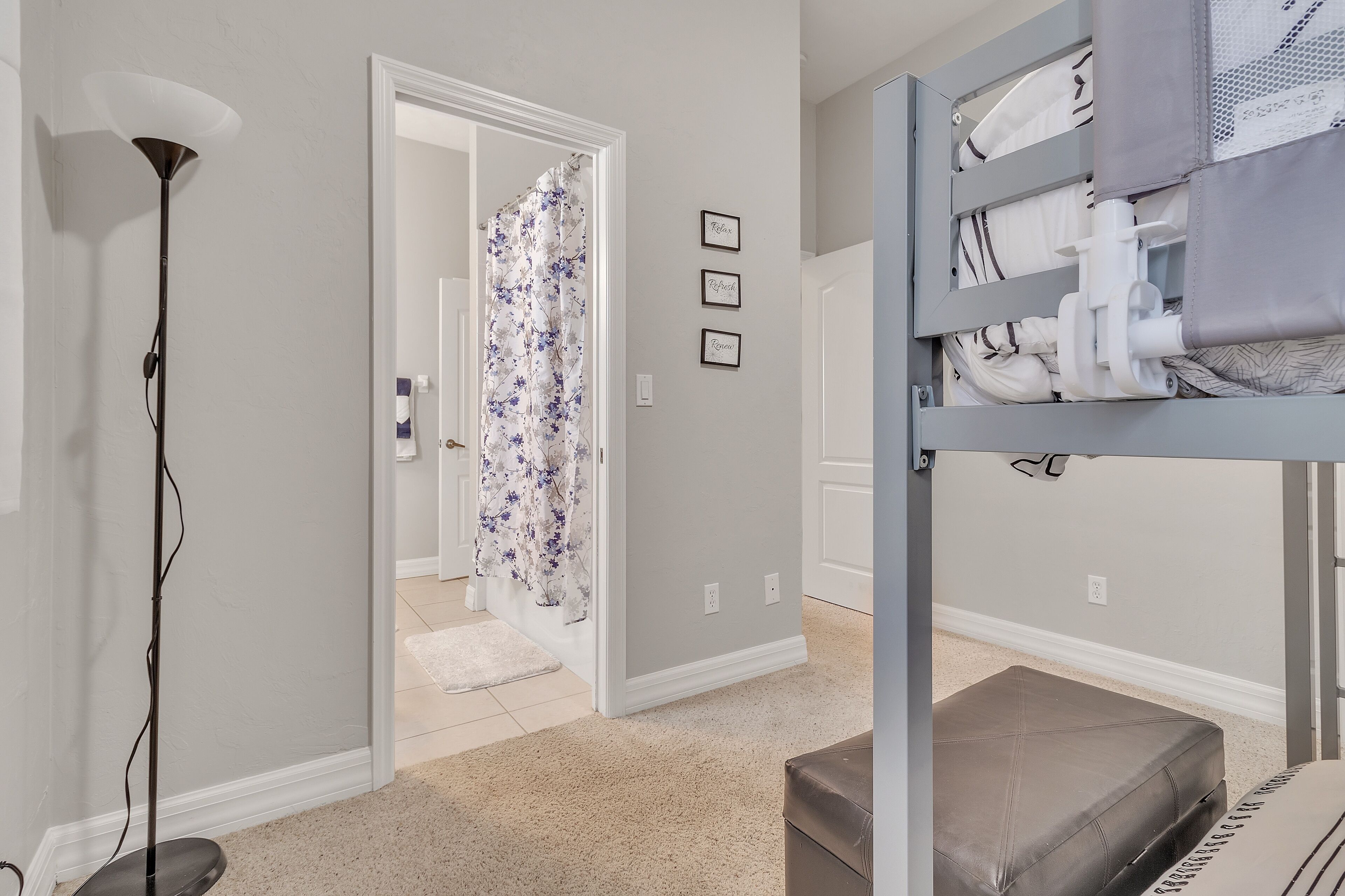 A room with a bunk bed, a floor lamp, and a shower with a floral curtain.