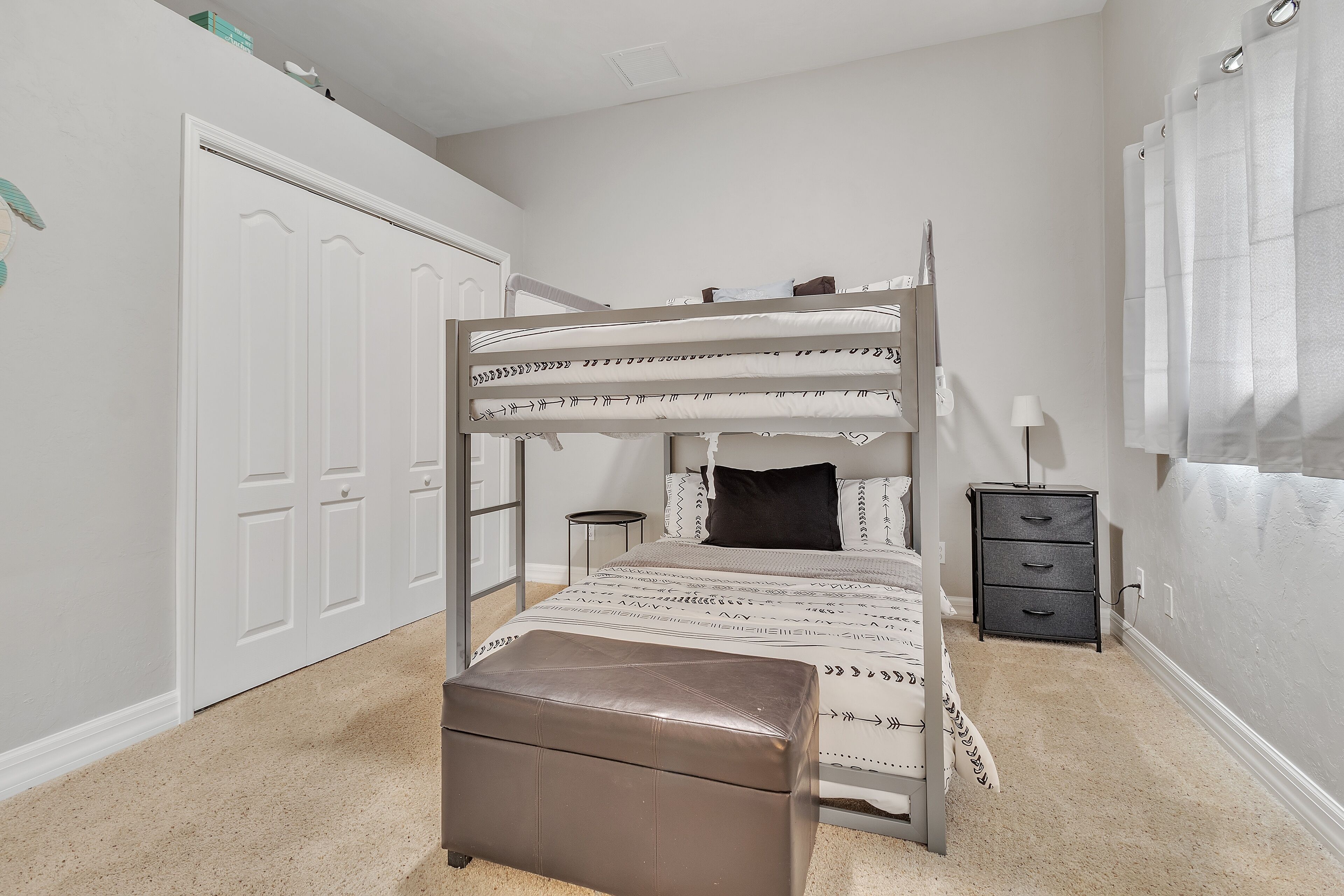 A bunk bed with a bedside table and a lamp, a door, and a window with curtains.