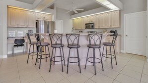 A modern kitchen with five bar stools, a ceiling fan, and a large island. - Blue Oasis 3 Bedroom Home by RedAwning (Cape Coral)