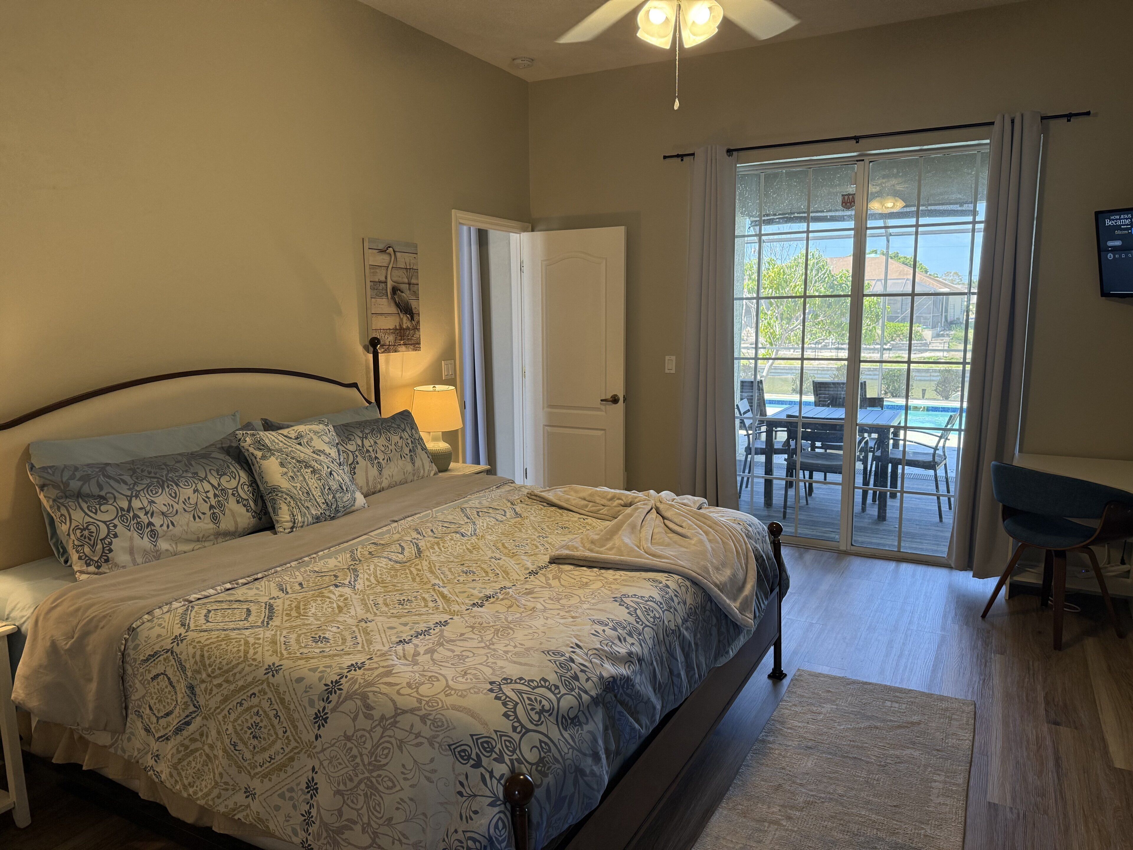 A bedroom with a bed, a nightstand, a lamp, a door leading to a balcony, and a TV mounted on the wall.