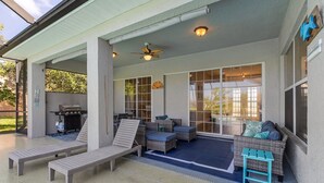 A covered outdoor seating area with lounge chairs, a small table, and a ceiling fan. - Blue Oasis 3 Bedroom Home by RedAwning (Cape Coral)