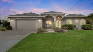 A single-story house with a garage, a front porch, and a well-maintained lawn. - Blue Oasis 3 Bedroom Home by RedAwning (Cape Coral)