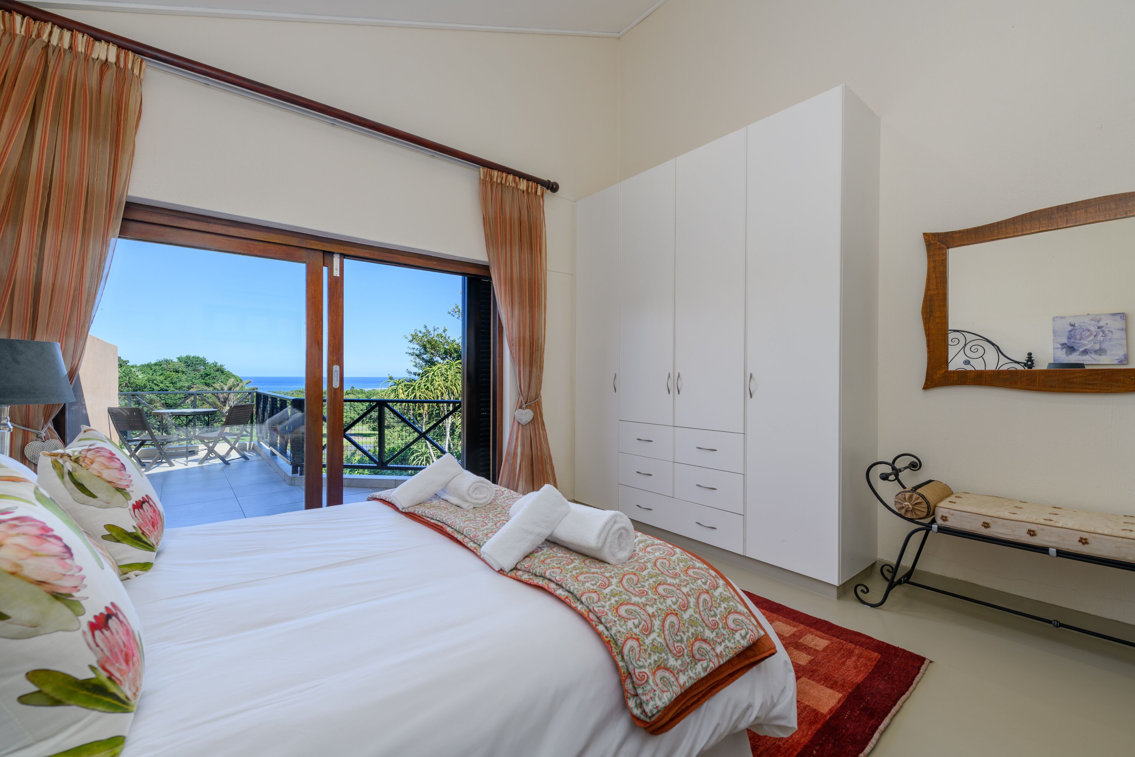 A bedroom with a bed, a wardrobe, a bench, and a view of the outdoors.