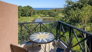 A balcony with a mosaic table, two wooden chairs, and a view of a golf course and ocean. - San Lameer Villa 14214 (Southbroom)