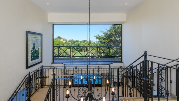 A staircase with a wrought iron railing, a chandelier, and a large window with a view of a green landscape. - San Lameer Villa 14214 (Southbroom)