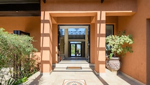 A building entrance with a tiled pathway leading to a door, flanked by plants and a large potted tree. - San Lameer Villa 14214 (Southbroom)