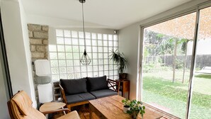 A cozy room with a wooden table, a sofa, and chairs. There's a large window with a view of a garden. - Villa Accueillante et Familiale (La Garde)
