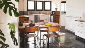 A modern kitchen with a dining area, featuring a central island, wooden chairs, and a white countertop. - Villa Accueillante et Familiale (La Garde)