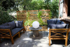 Relax in this charming outdoor seating area with a wooden bench and two chairs, surrounded by lush greenery and a rustic wooden fence.