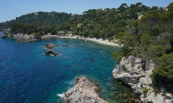 Experience the serene coastal landscape with a clear blue sea, rocky outcrops, and lush greenery.