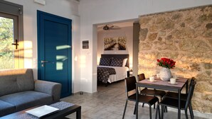 A modern hotel room with a blue door, a bed with star-patterned bedding, a dining area with a table and chairs, and a stone wall. - Gems Apartments (Corfu)