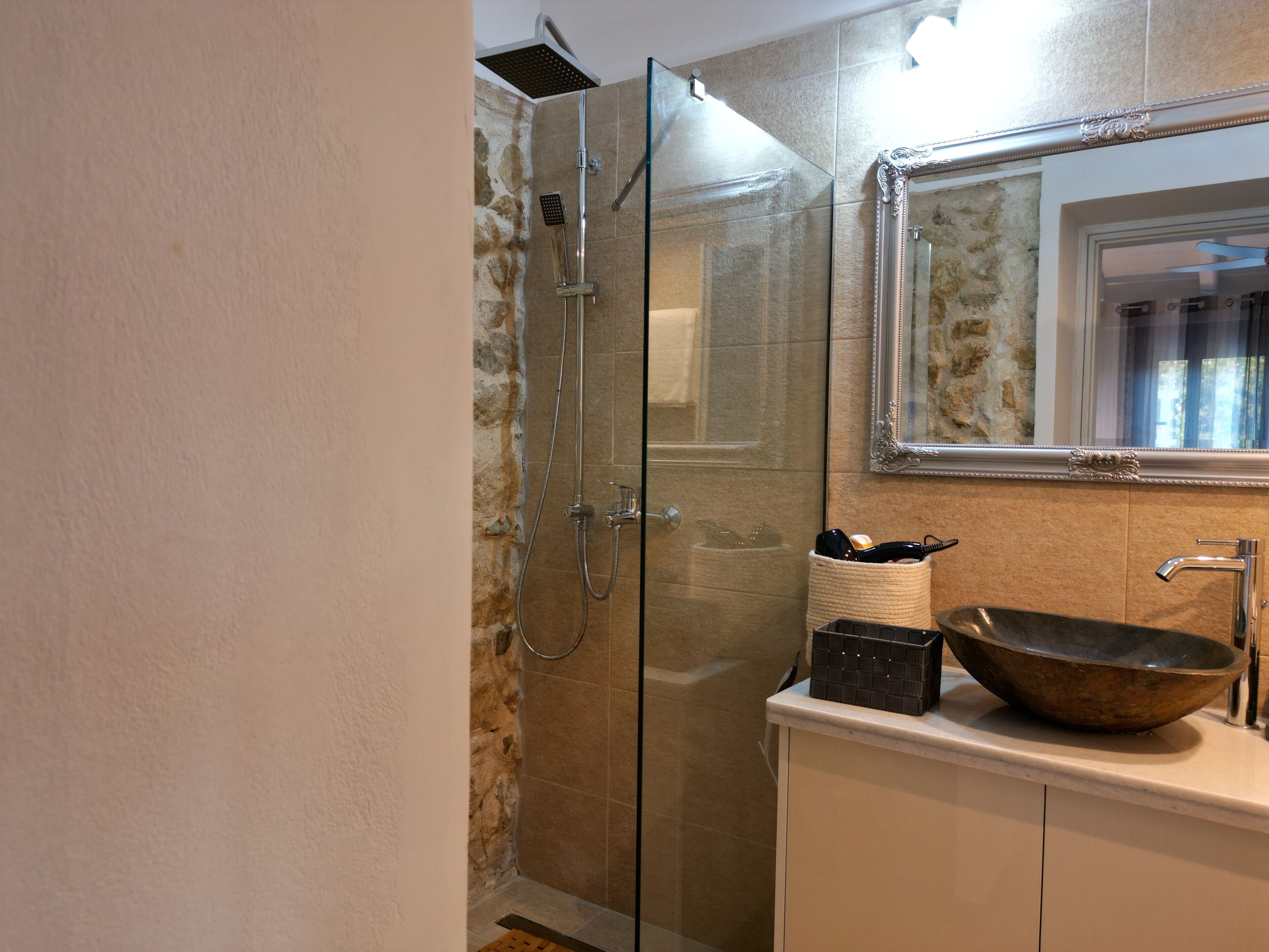 A bathroom with a glass-enclosed shower, a sink with a large bowl, and a mirror with an ornate frame.