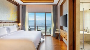 A hotel room with a large bed, a TV, a bathroom with a bathtub, and a view of mountains through the window. - Dusit Thani Himalayan Resort Dhulikhel Nepal (Dhulikhel)