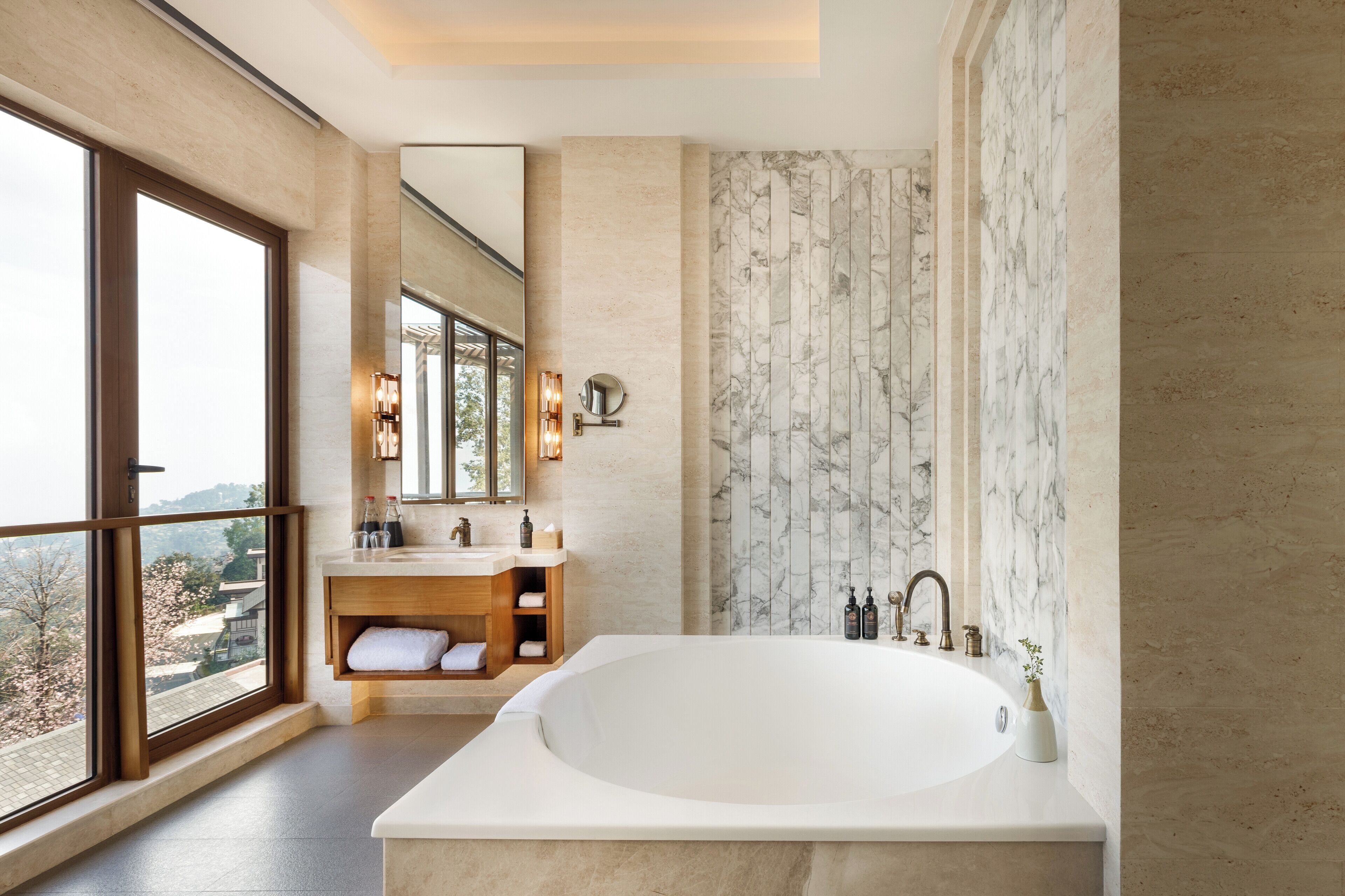 Un baño moderno con una bañera grande, un tocador de madera, un espejo amplio y vistas al exterior.