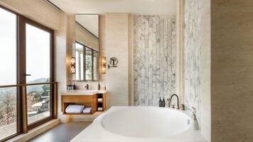Un baño moderno con una bañera grande, un tocador de madera, un espejo amplio y vistas al exterior.