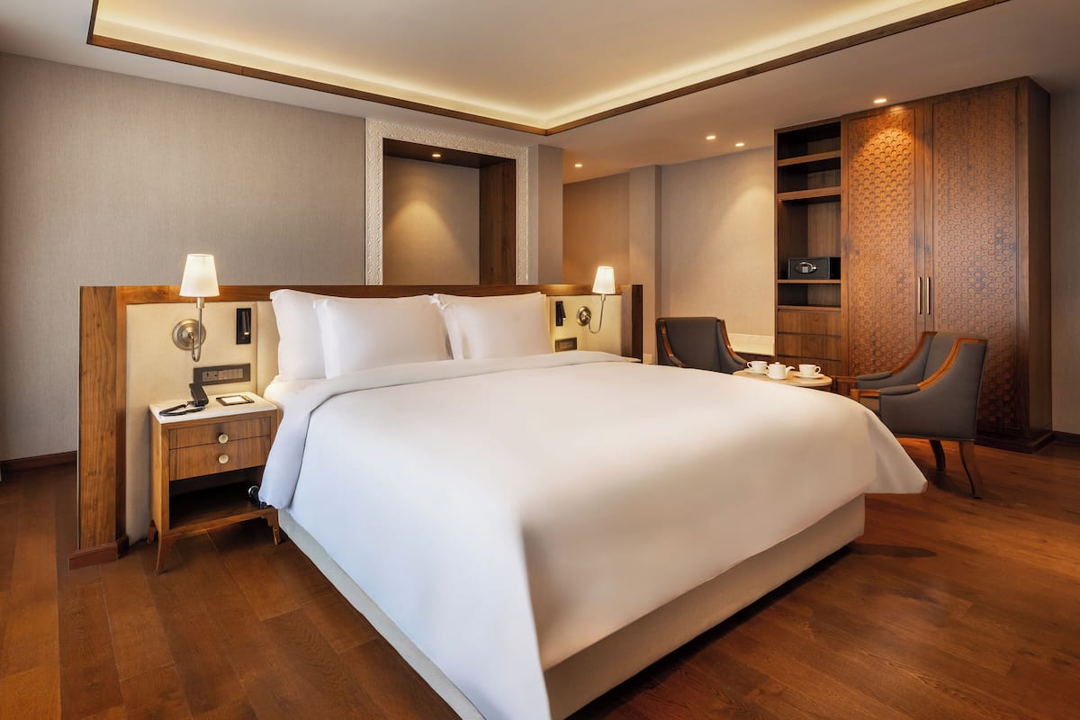 A hotel room with a large bed, bedside tables with lamps, a wardrobe, and a seating area with a chair and table.