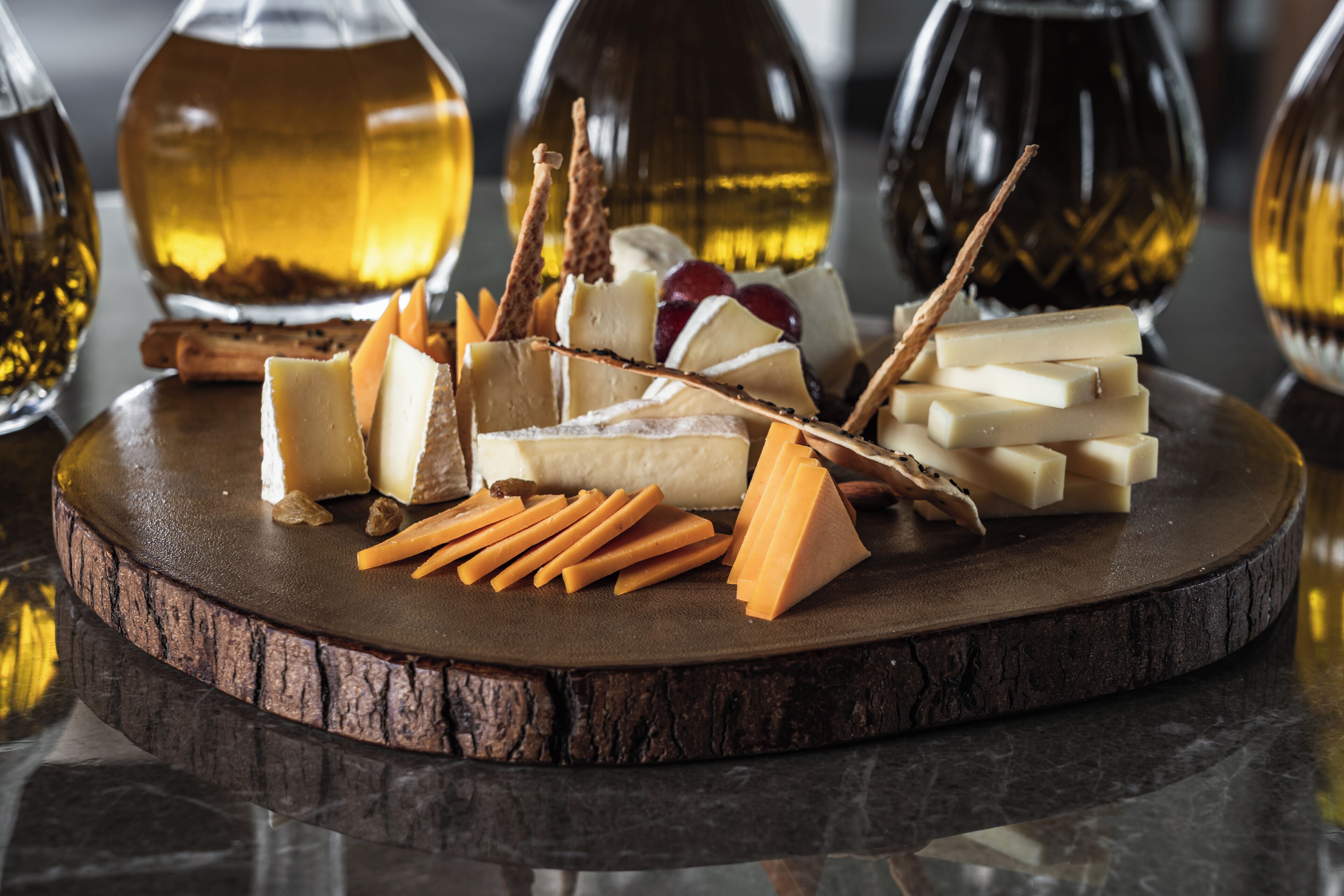 A wooden board with various cheeses, crackers, and grapes.