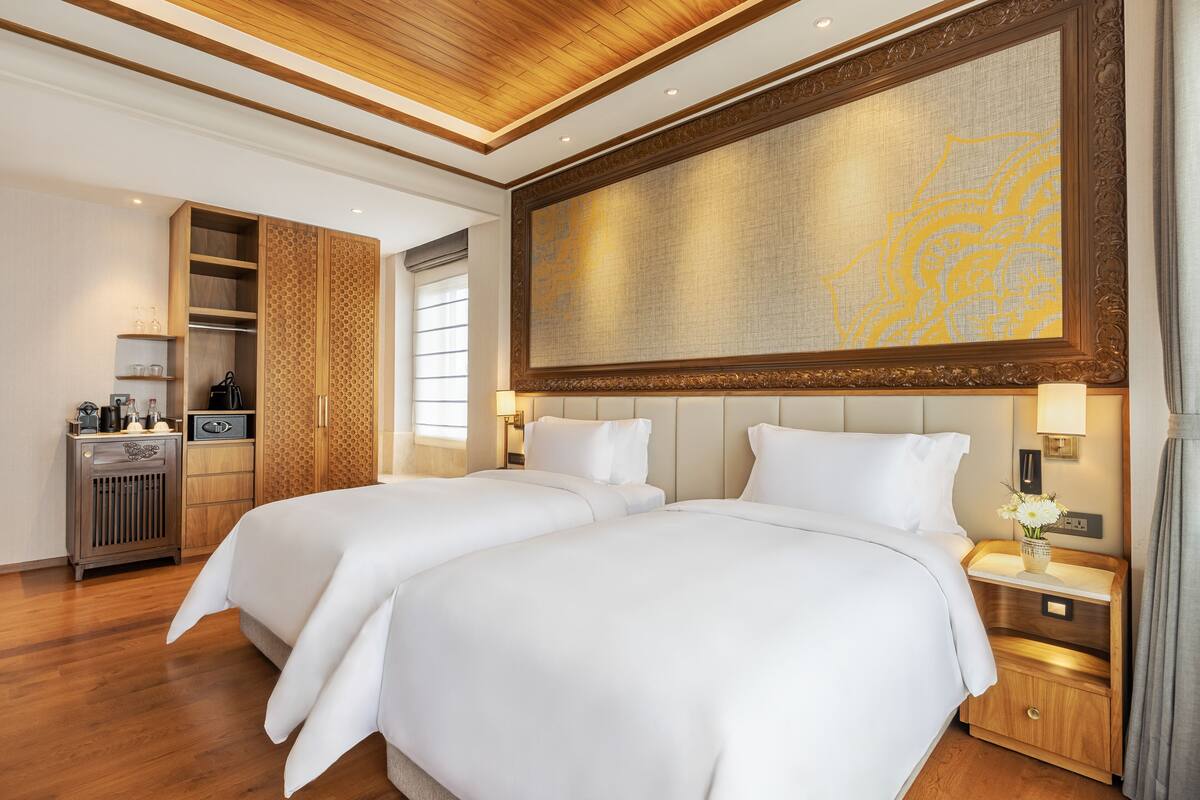 A hotel room with two beds, a wardrobe, a minibar, and a large decorative wall.