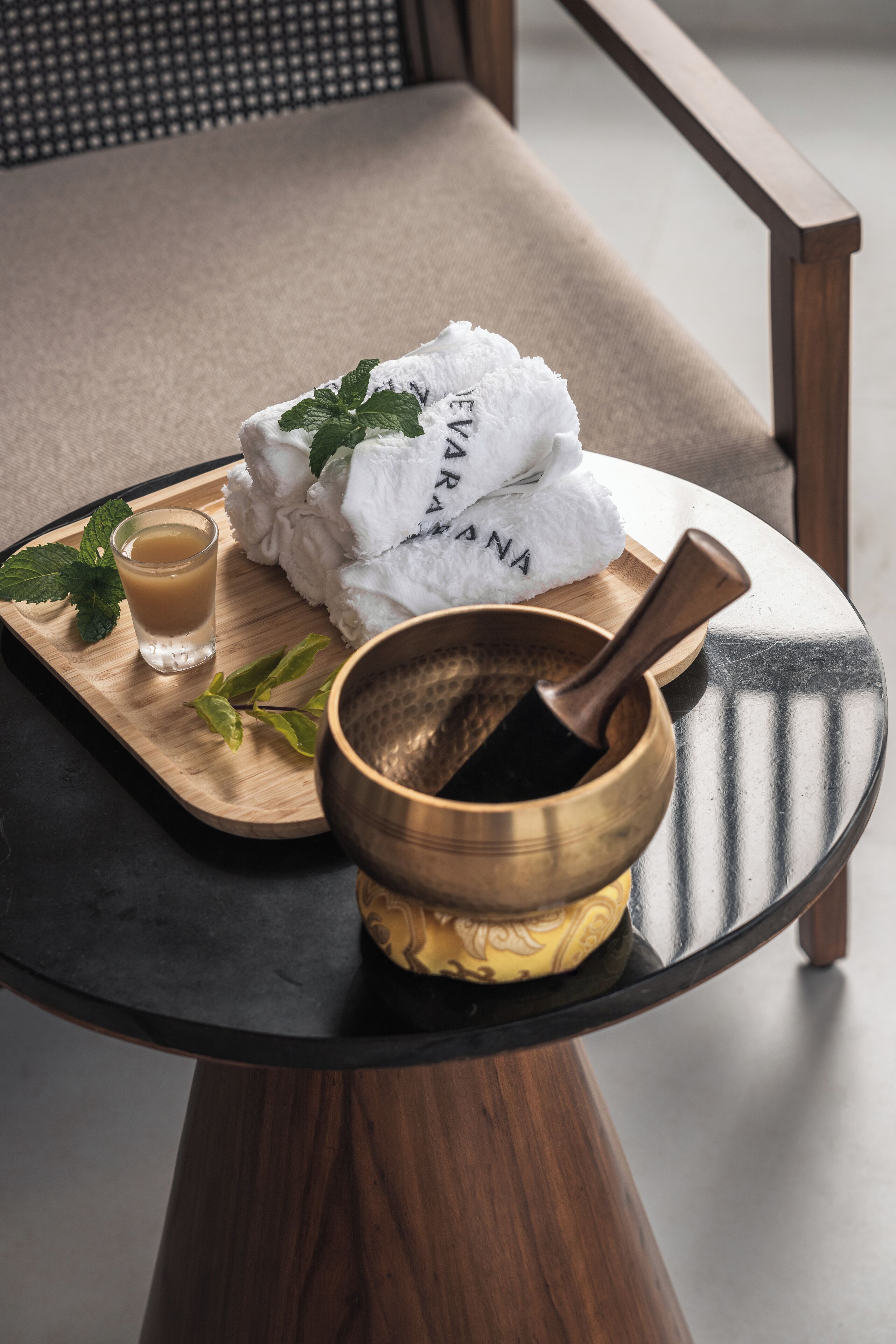 A wooden tray with a shot glass, a mortar and pestle, and a stack of white towels with mint leaves on a round table.