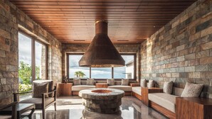 A spacious living area with a stone fireplace, wooden ceiling, and large windows offering a view of the outdoors. - Dusit Thani Himalayan Resort Dhulikhel Nepal (Dhulikhel)