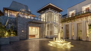 A modern building with a stone facade, a central courtyard with a water feature, and a balcony with plants. - Dusit Thani Himalayan Resort Dhulikhel Nepal (Dhulikhel)