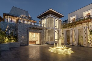 A modern building with a stone facade, a central courtyard with a water feature, and a balcony with plants.