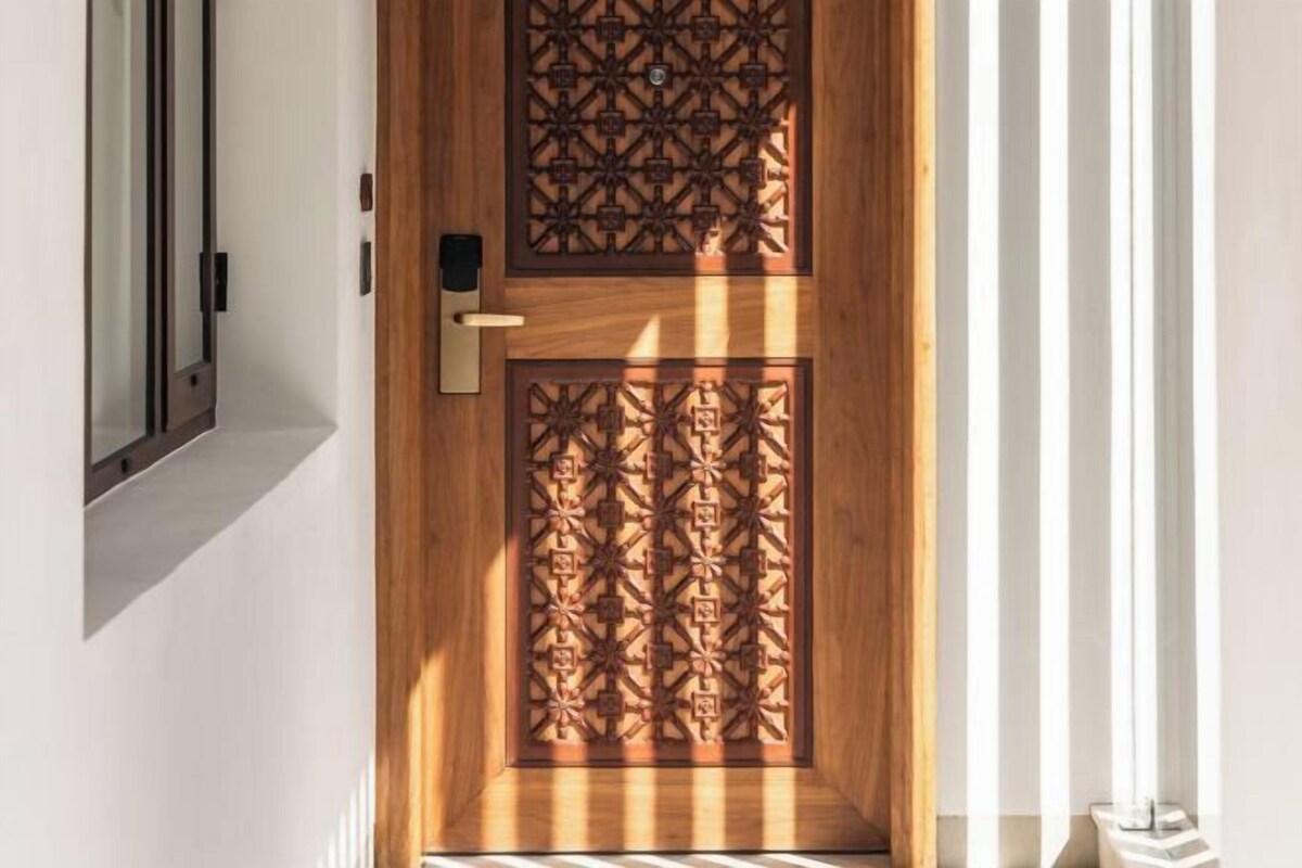 Una puerta de madera con intrincados diseños geométricos y un picaporte moderno.