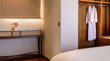 Habitación de hotel con una cama grande, piso de madera, tocador con espejo y un armario de madera con una bata colgada.