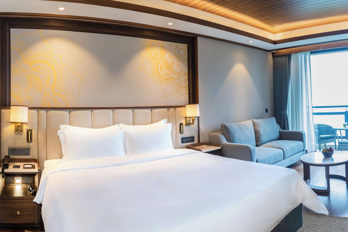 A hotel room with a large bed, a sofa, a small table, and a view of the outdoors.