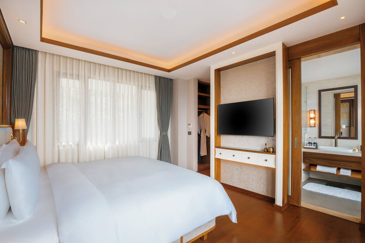 A hotel room with a large bed, a TV, a vanity with a mirror, and a walk-in closet.