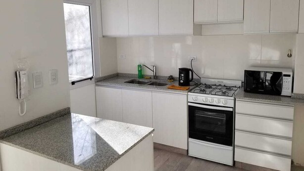 Pieni, käytännöllinen keittiö, jossa on valkoiset kaapit, kaasuliesi, uuni, mikroaaltouuni ja pesuallas.