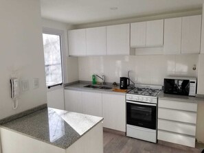 A compact kitchen with white cabinets, a gas stove, an oven, a microwave, and a sink. - Departamento Nuevo Ideal Familia, Mendoza, a Minutos del Centro (Godoy cruz)