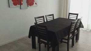 Ruokailutilassa on suorakaiteen muotoinen pöytä ja kuusi tuolia, seinälle asennettu ilmastointilaite sekä ikkuna, jossa on verhot.