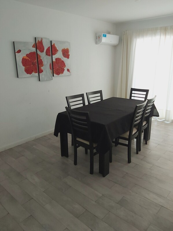 A dining area with a rectangular table and six chairs, a wall-mounted air conditioner, and a window with curtains. - Departamento Nuevo Ideal Familia, Mendoza, a Minutos del Centro (Godoy cruz)