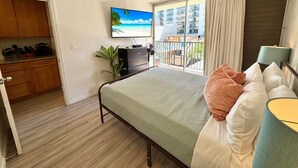 A bedroom with a bed, a dresser, a TV, a balcony with a view of buildings, and a plant. - Relaxing Kalakauan 1-Bedroom | Recently Redecorated! (Honolulu)